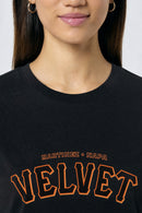 Person wearing a black t-shirt with 'Velvet' printed in orange on a light background
