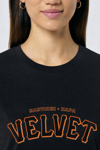 Person wearing a black t-shirt with 'Velvet' printed in orange on a light background