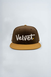 Brown and beige cap with 'Velvet' logo on a light gray background