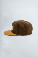 Brown and mustard yellow cap with a logo on a light gray background