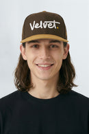 Person wearing a brown cap with 'Velvet' logo on a light gray background