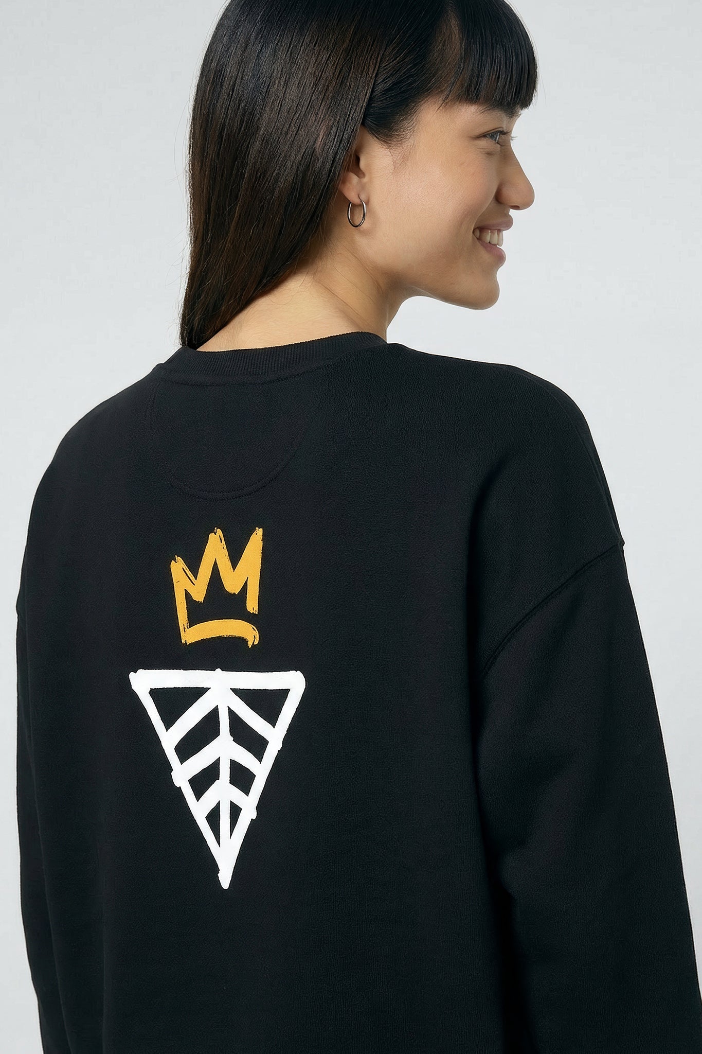 Person wearing a black sweatshirt with a logo on the back against a light background