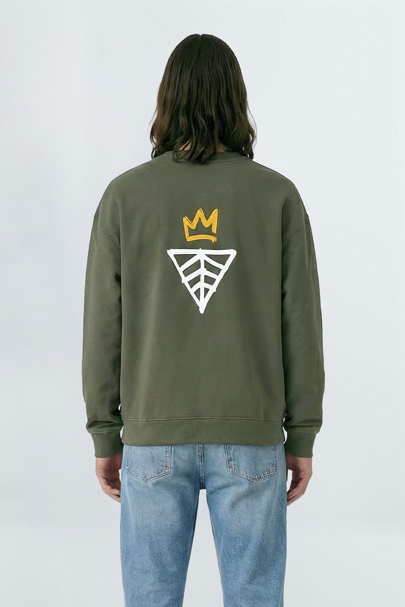 Person wearing a khaki green sweatshirt with a logo on the back against a light background