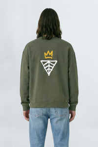 Person wearing a khaki green sweatshirt with a logo on the back against a light background