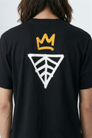 Black t-shirt with a yellow crown and geometric design on the back, worn by a person.