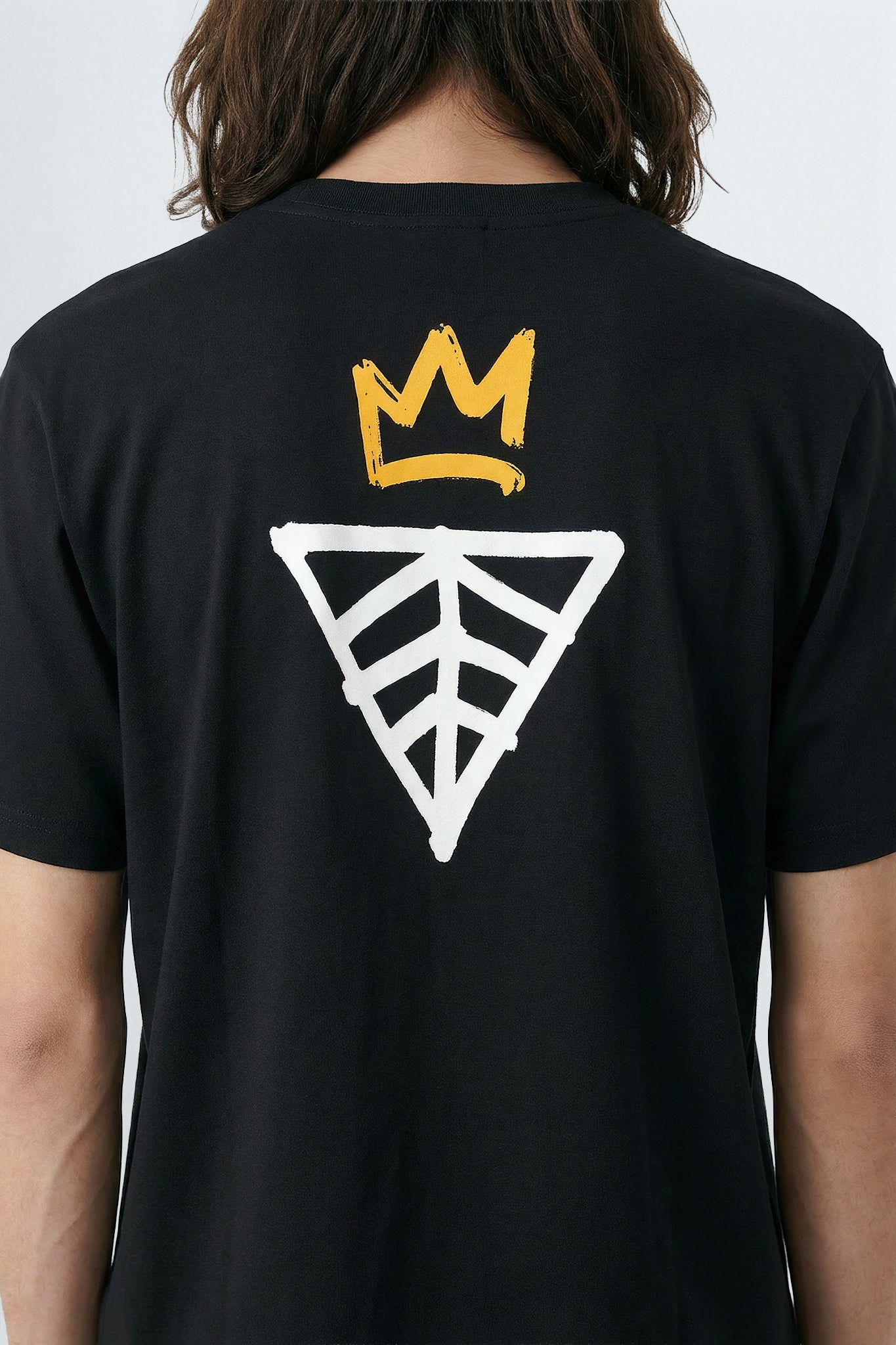 Black t-shirt with a yellow crown and geometric design on the back, worn by a person.