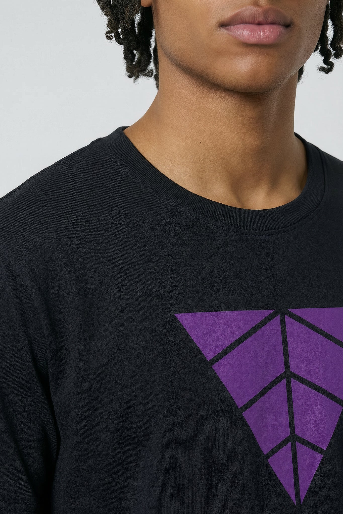 Person wearing a black t-Shirt with a purple geometric logo on a plain background