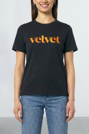 Person wearing a black t-shirt with 'velvet' printed in orange on a plain background