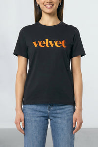 Person wearing a black t-shirt with 'velvet' printed in orange on a plain background