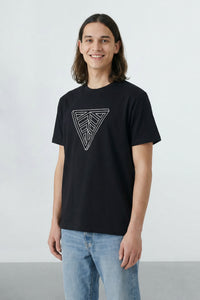 Person wearing a black t-shirt with a geometric design on a plain background