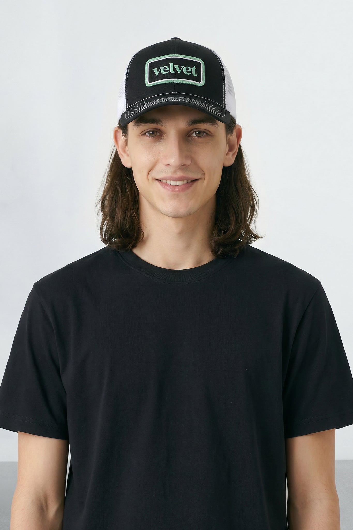 Person wearing a black cap with 'velvet' logo and black t-shirt against a light background