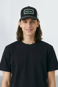 Person wearing a black cap with 'velvet' logo and black t-shirt against a light background