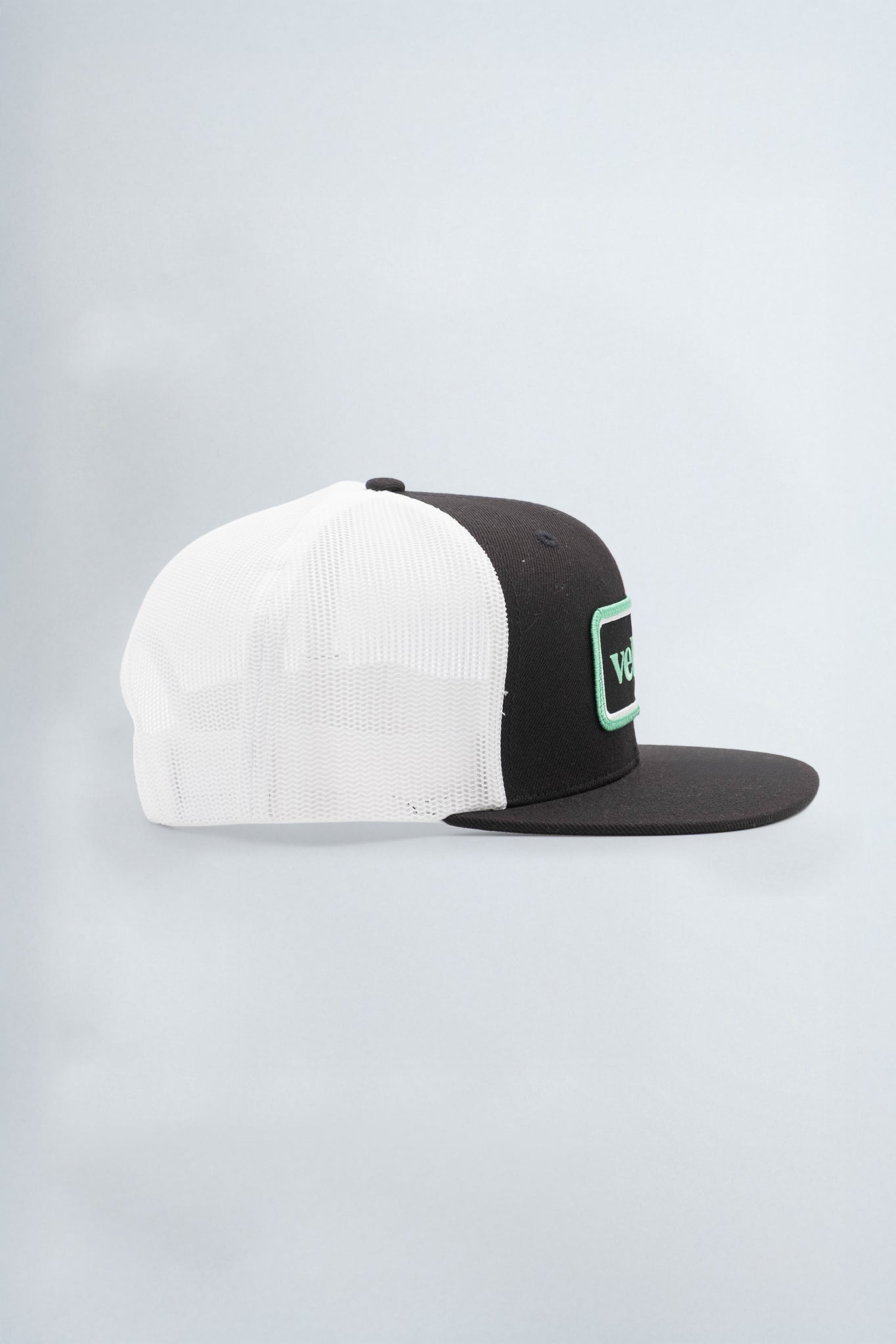 Two-tone black and white cap with a green logo on a light background