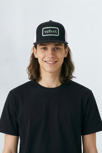Person wearing a black cap with 'velvet' logo on a background