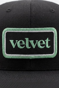 Black cap with a green 'velvet' patch on a white background