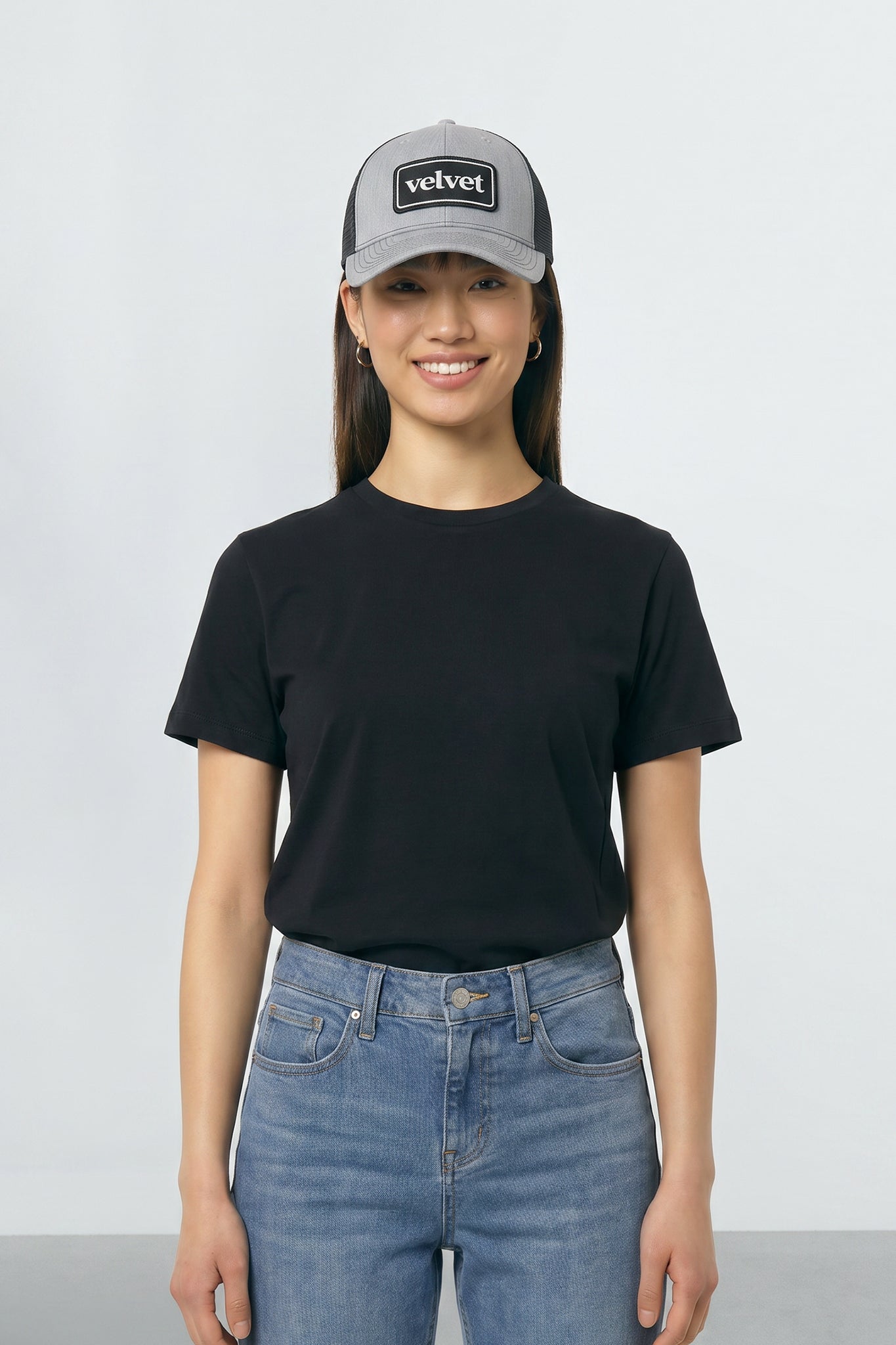 Person wearing a black t-shirt, blue jeans, and a gray cap with 'velvet' branding on a white background
