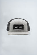 Gray and black trucker cap with 'velvet' logo on a light gray background