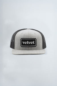 Gray and black trucker cap with 'velvet' logo on a light gray background