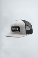 Gray and black trucker hat with 'velvet' logo on a light gray background