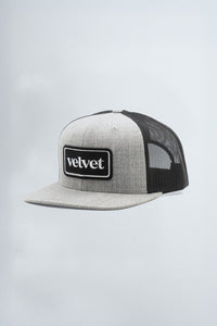 Gray and black trucker hat with 'velvet' logo on a light gray background