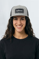 Woman wearing a gray and black cap with 'velvet' logo on a white background