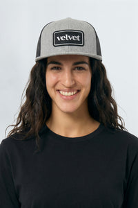 Woman wearing a gray and black cap with 'velvet' logo on a white background