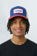 Person wearing a blue and red cap with 'velvet' logo on a white background