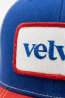 Close-up of a blue and red cap with 'velvet' branding on a white patch.