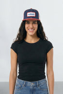 Woman wearing a black t-shirt and blue jeans with a navy and red cap on a white background