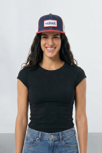 Woman wearing a black t-shirt and blue jeans with a navy and red cap on a white background