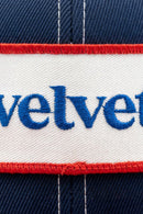 Close-up of a cap with 'velvet' embroidered on it, featuring red, white, and blue colors.