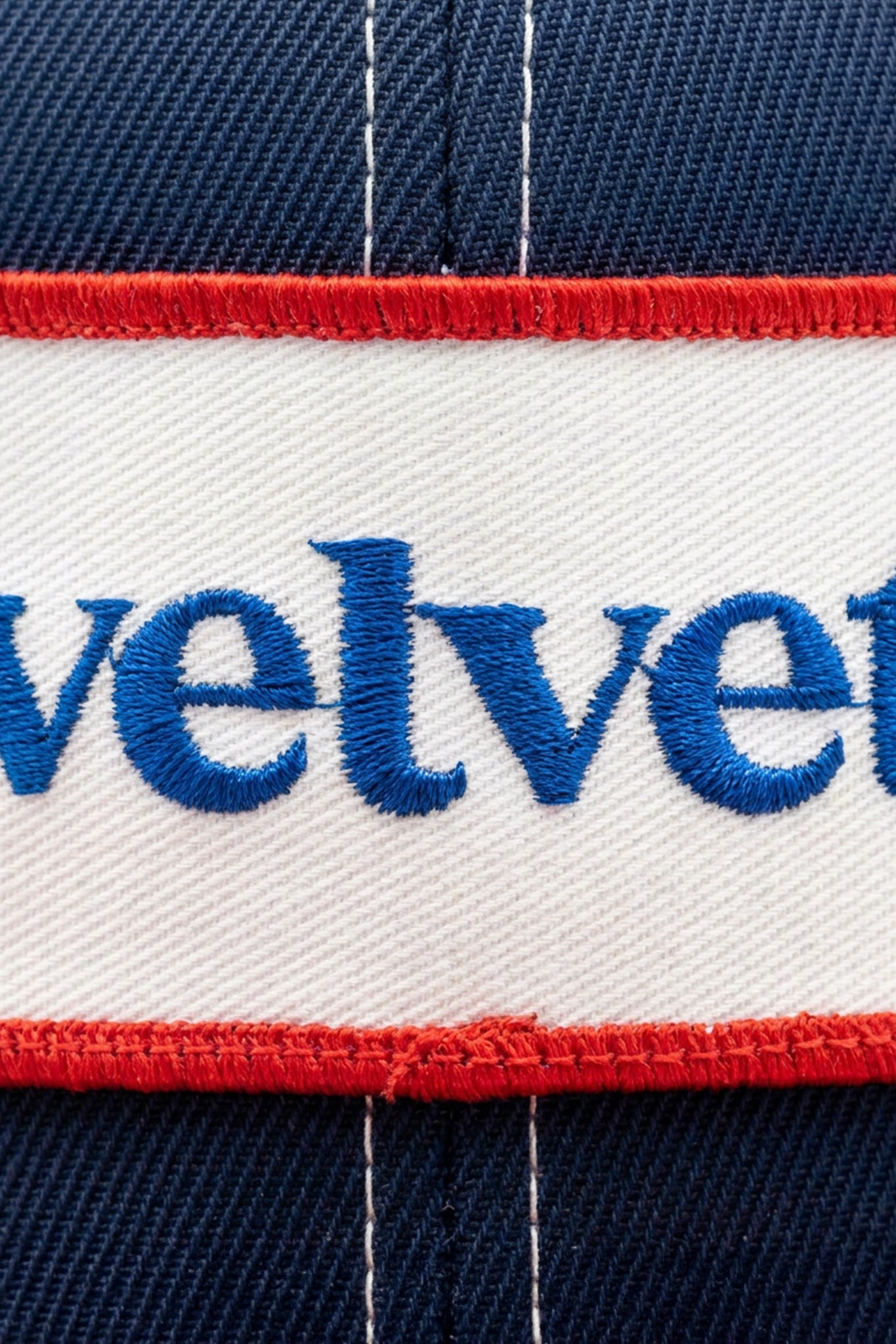 Close-up of a cap with 'velvet' embroidered on it, featuring red, white, and blue colors.
