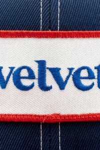 Close-up of a cap with 'velvet' embroidered on it, featuring red, white, and blue colors.