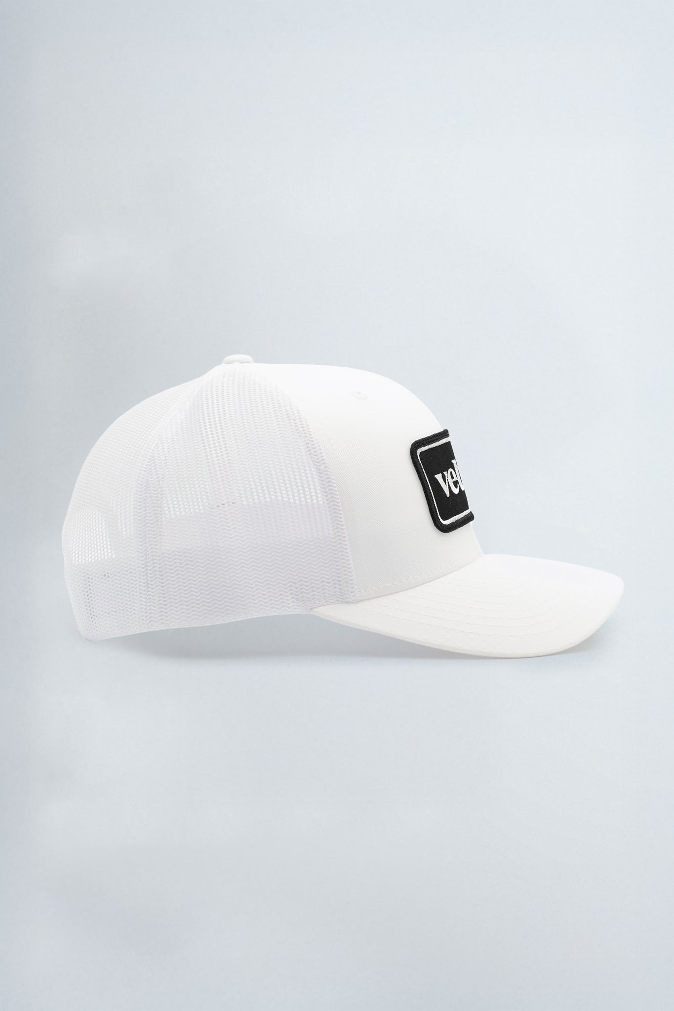 White cap with a black logo patch on a light background