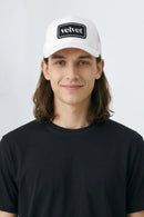 Person wearing a white cap with 'velvet' logo on a plain background