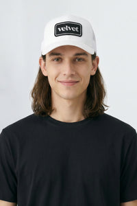Person wearing a white cap with 'velvet' logo on a plain background