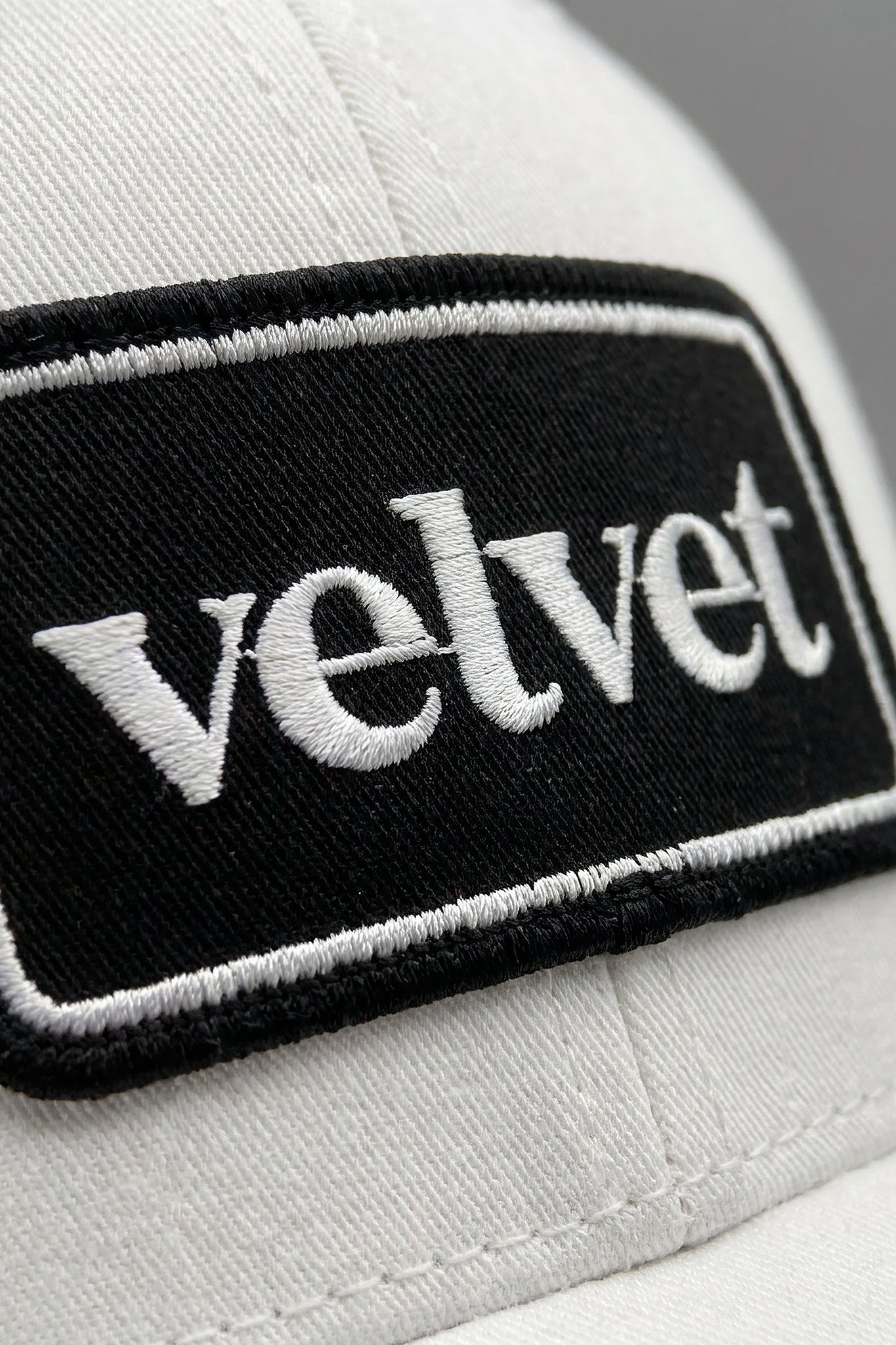 White cap with a black patch displaying the word 'velvet'.