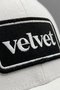 White cap with a black patch displaying the word 'velvet'.