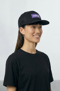 Person wearing a black cap with 'velvet' logo on a light  background