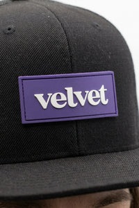 Black cap with a purple 'velvet' patch on a blurred background
