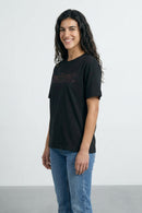 Woman wearing a black t-shirt with text and blue jeans on a light background