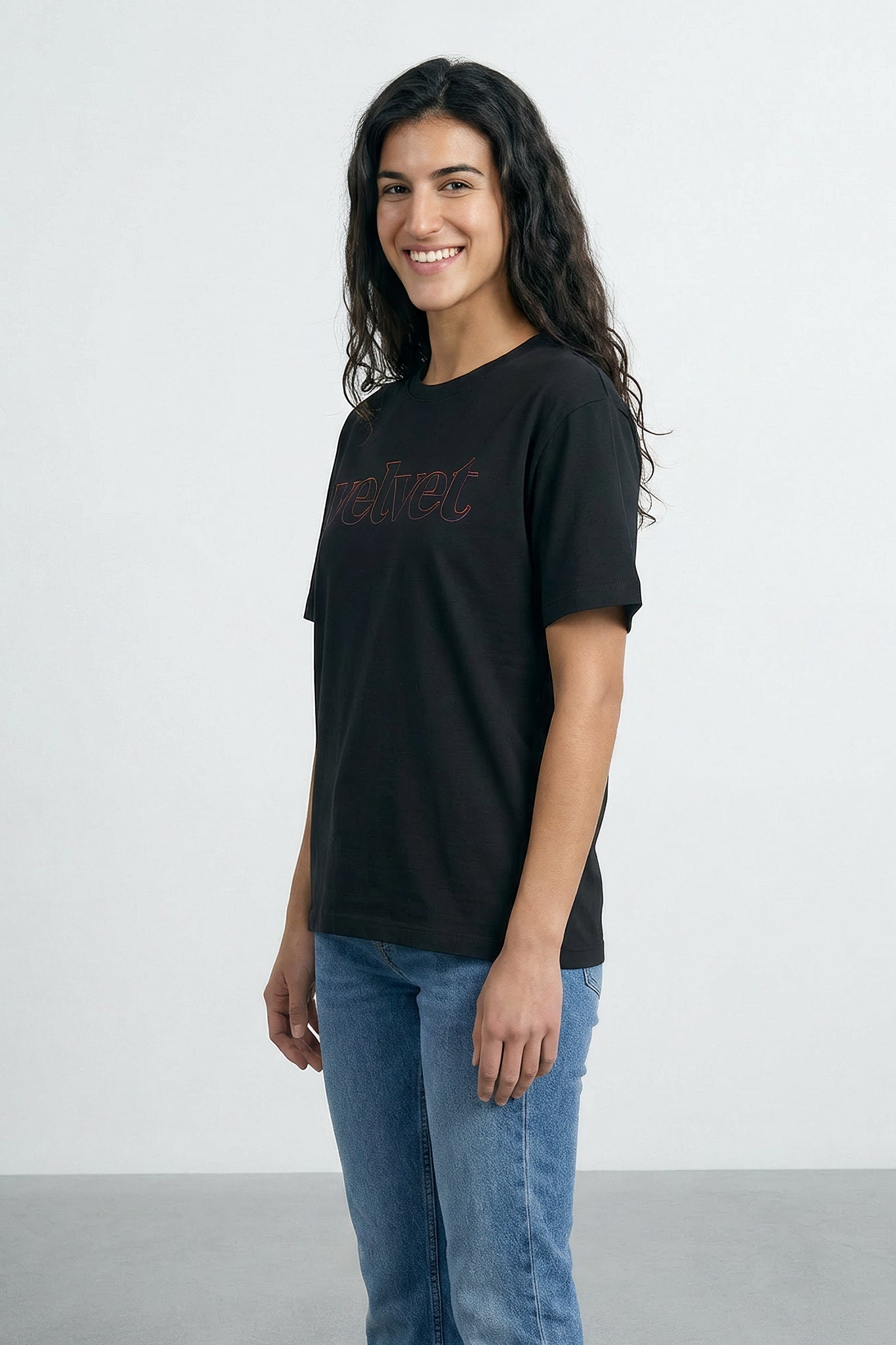 Woman wearing a black t-shirt with text and blue jeans on a light background