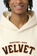 Person wearing a cream hoodie with 'Martinez + Napa Velvet' text on a light background