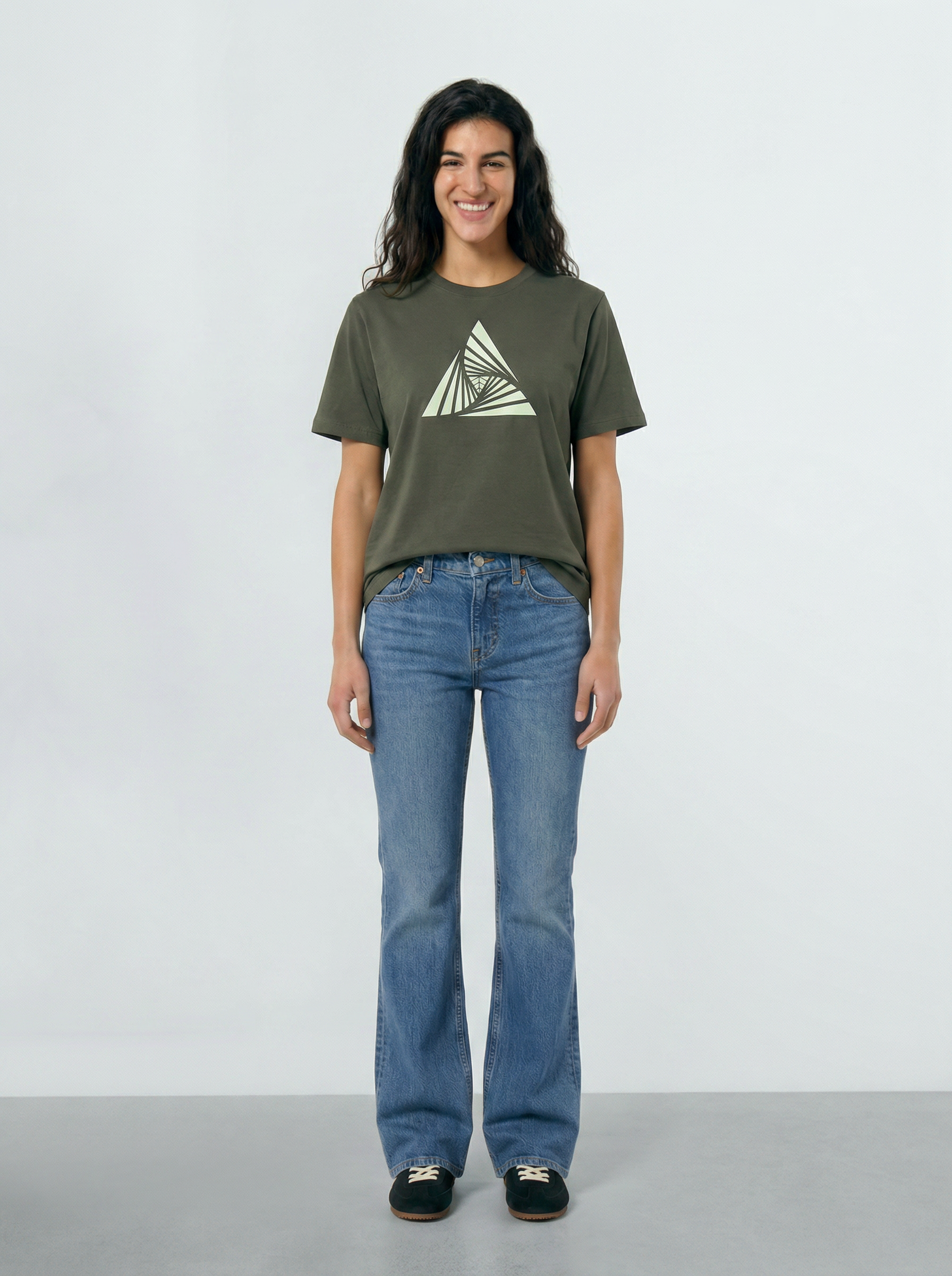 Person wearing a Khaki green t-shirt with a triangle design and blue jeans on a light background